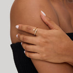 A person with light brown skin wears a black textured strapless top and the Crystal Shooting Star Open Ring in Gold, featuring a small stone, gently resting a hand on their bare shoulder. Their nails are manicured with pale polish.