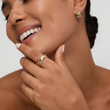 A smiling woman with smooth skin wears the Mia Two-tone Mixed Metal Hoops. She gently touches her chin, highlighting her everyday jewellery and natural beauty, with her hair pulled back and eyes closed.