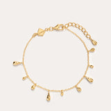 The Rhea Molten Cascade Bracelet in Gold features small teardrop-shaped charms with a subtle hammered texture, each charm evenly spaced along the 14K gold plated chain and finished with an adjustable clasp, displayed on a plain light background.