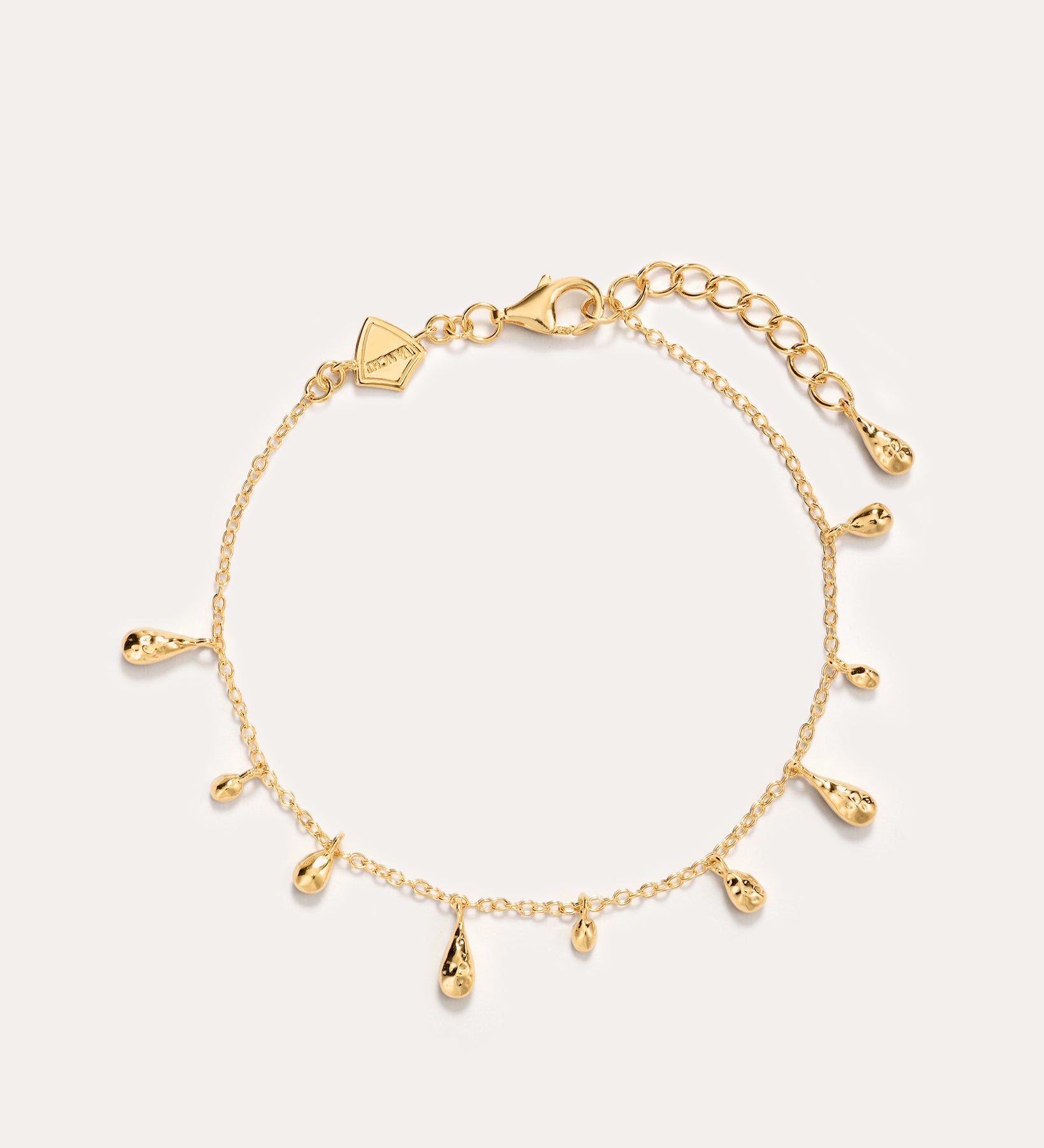 The Rhea Molten Cascade Bracelet in Gold features small teardrop-shaped charms with a subtle hammered texture, each charm evenly spaced along the 14K gold plated chain and finished with an adjustable clasp, displayed on a plain light background.