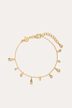 The Rhea Molten Cascade Bracelet in Gold features small teardrop-shaped charms with a subtle hammered texture, each charm evenly spaced along the 14K gold plated chain and finished with an adjustable clasp, displayed on a plain light background.