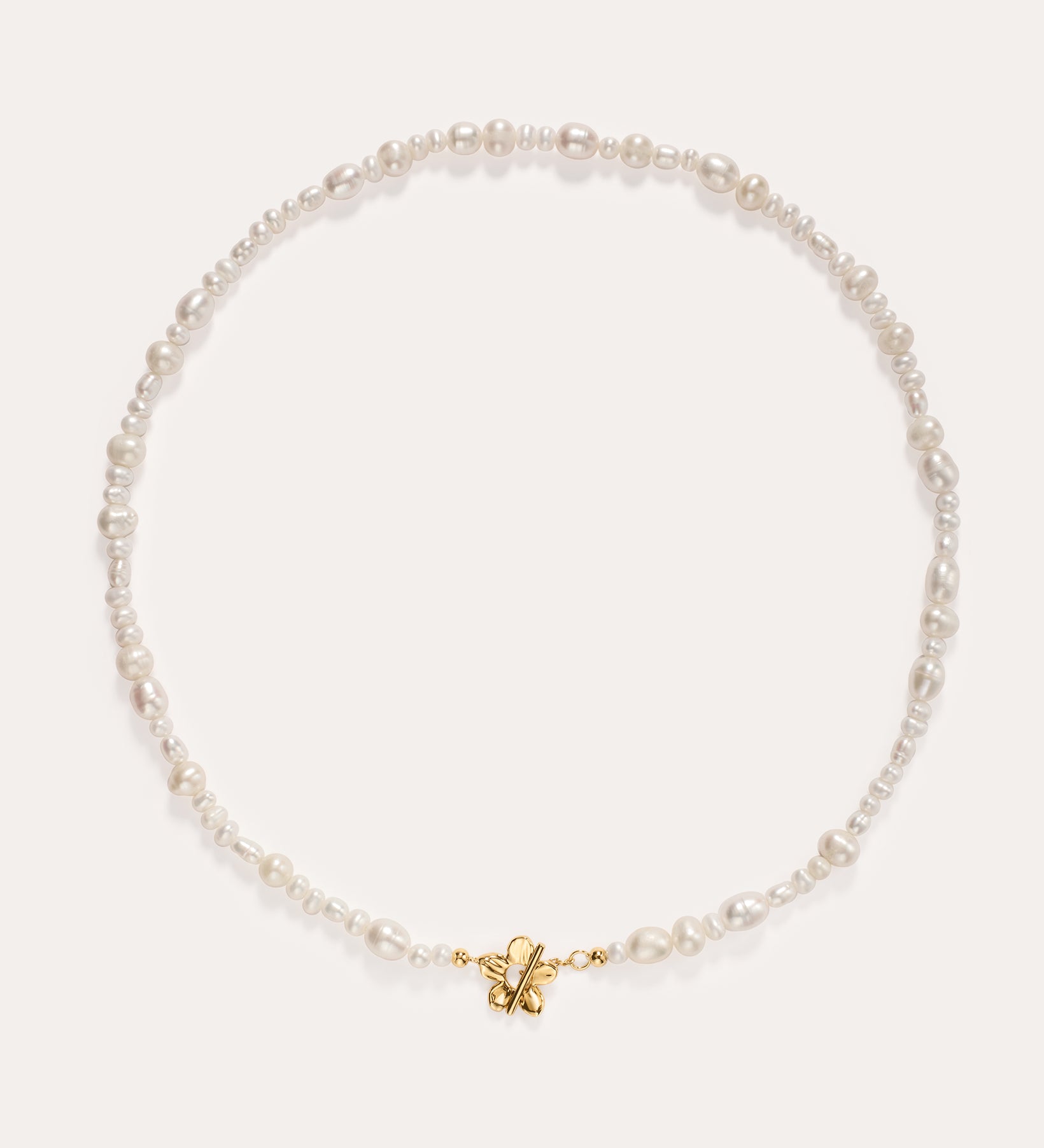 The Flora Multi Pearl Toggle Choker in Gold features irregularly shaped white freshwater pearls and a small 14K gold plated butterfly charm at the center, finished with a floral toggle clasp and displayed on a plain white background.