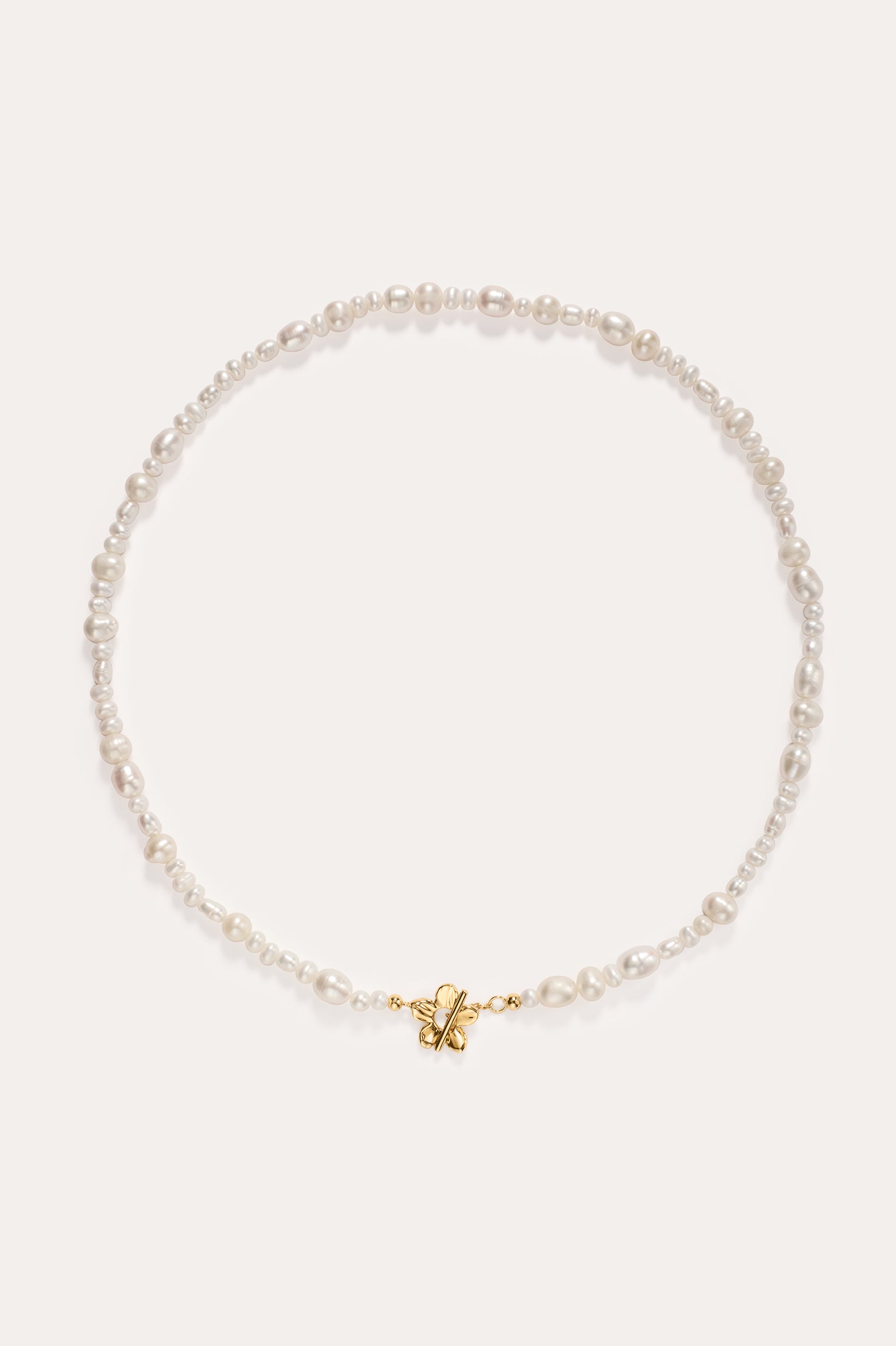 The Flora Multi Pearl Toggle Choker in Gold features irregularly shaped white freshwater pearls and a small 14K gold plated butterfly charm at the center, finished with a floral toggle clasp and displayed on a plain white background.