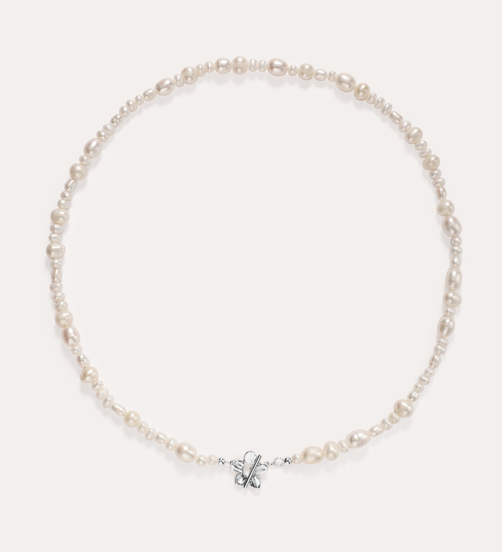 The Flora Multi Pearl Toggle Choker in Sterling Silver is a delicate piece featuring irregularly shaped freshwater pearls and a small sterling silver bow charm at the center, elegantly displayed on a plain light background.