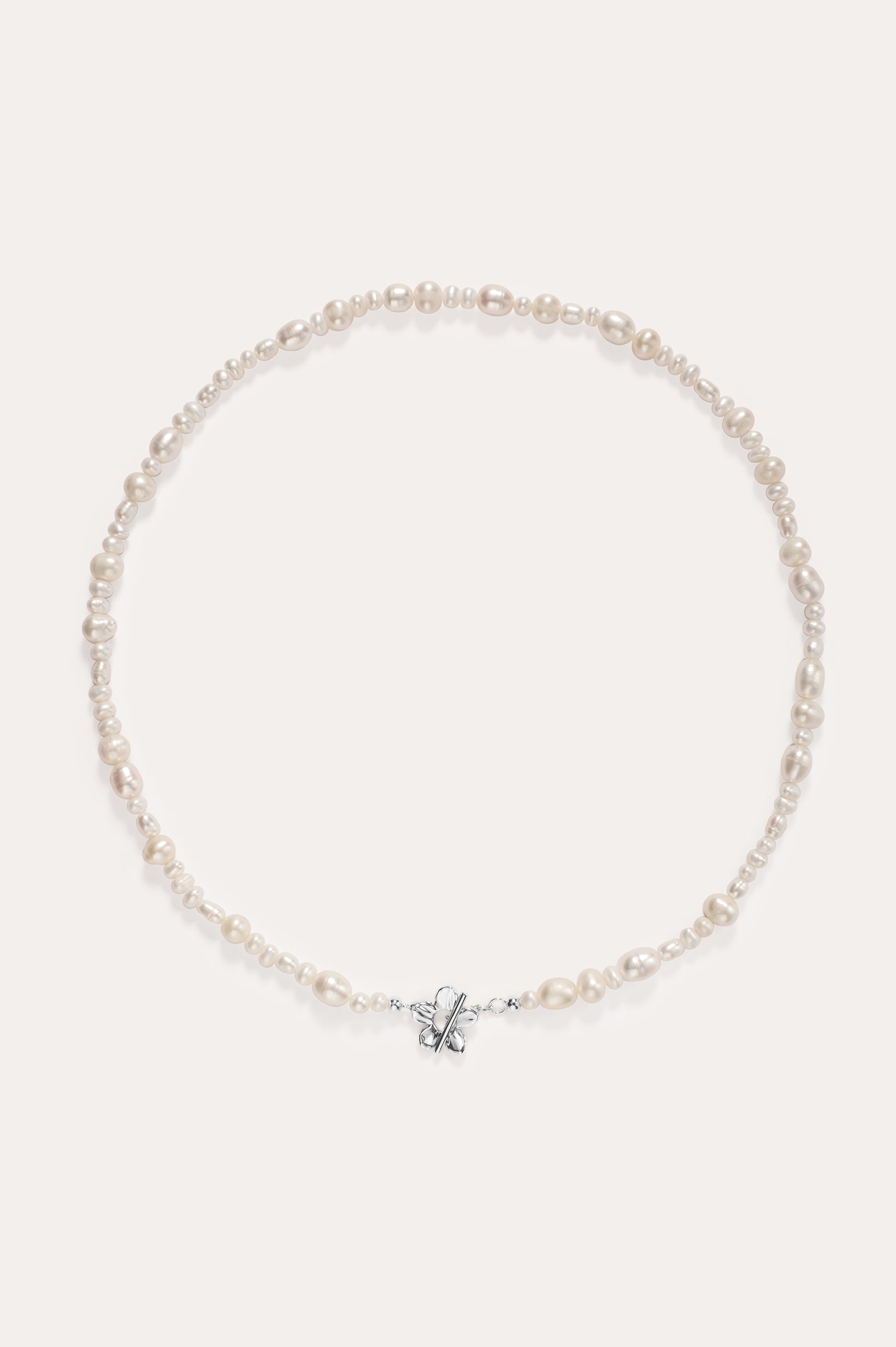 The Flora Multi Pearl Toggle Choker in Sterling Silver is a delicate piece featuring irregularly shaped freshwater pearls and a small sterling silver bow charm at the center, elegantly displayed on a plain light background.