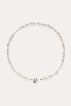 The Flora Multi Pearl Toggle Choker in Sterling Silver is a delicate piece featuring irregularly shaped freshwater pearls and a small sterling silver bow charm at the center, elegantly displayed on a plain light background.
