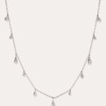 The Rhea Molten Cascade Necklace in Silver features small, teardrop-shaped charms with a subtle hammered texture, crafted from rhodium-plated metal and evenly spaced along a fine chain, displayed against a white background.