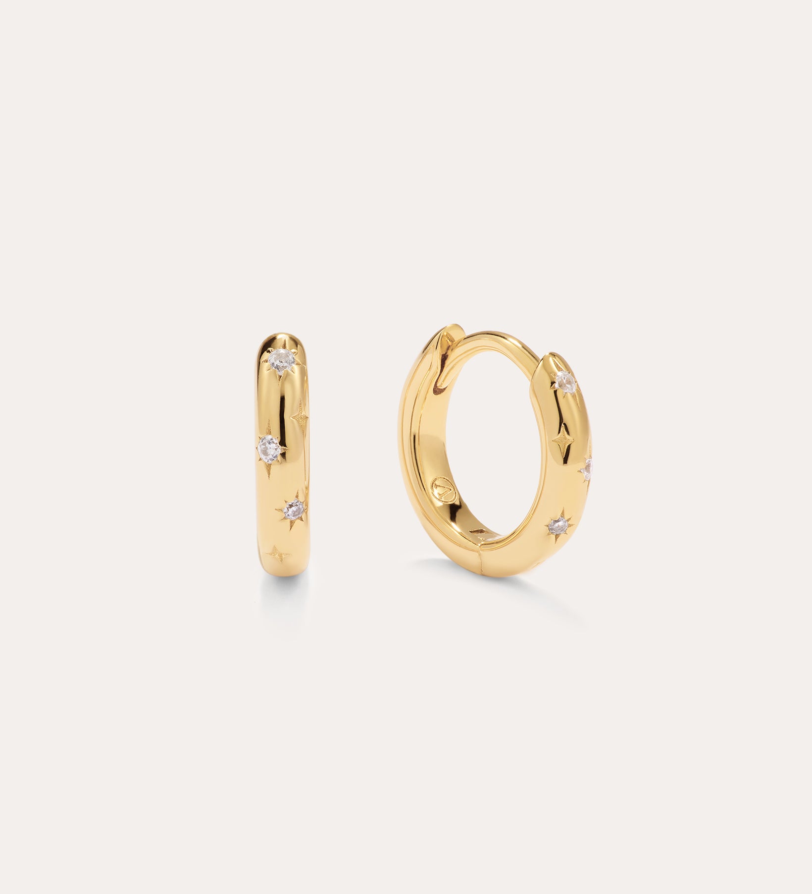A pair of Starfall Huggies in Gold, each featuring delicate star-shaped engravings and sparkling cubic zirconia gemstones, shown on a simple light background. These earrings add a touch of celestial charm to any ensemble.