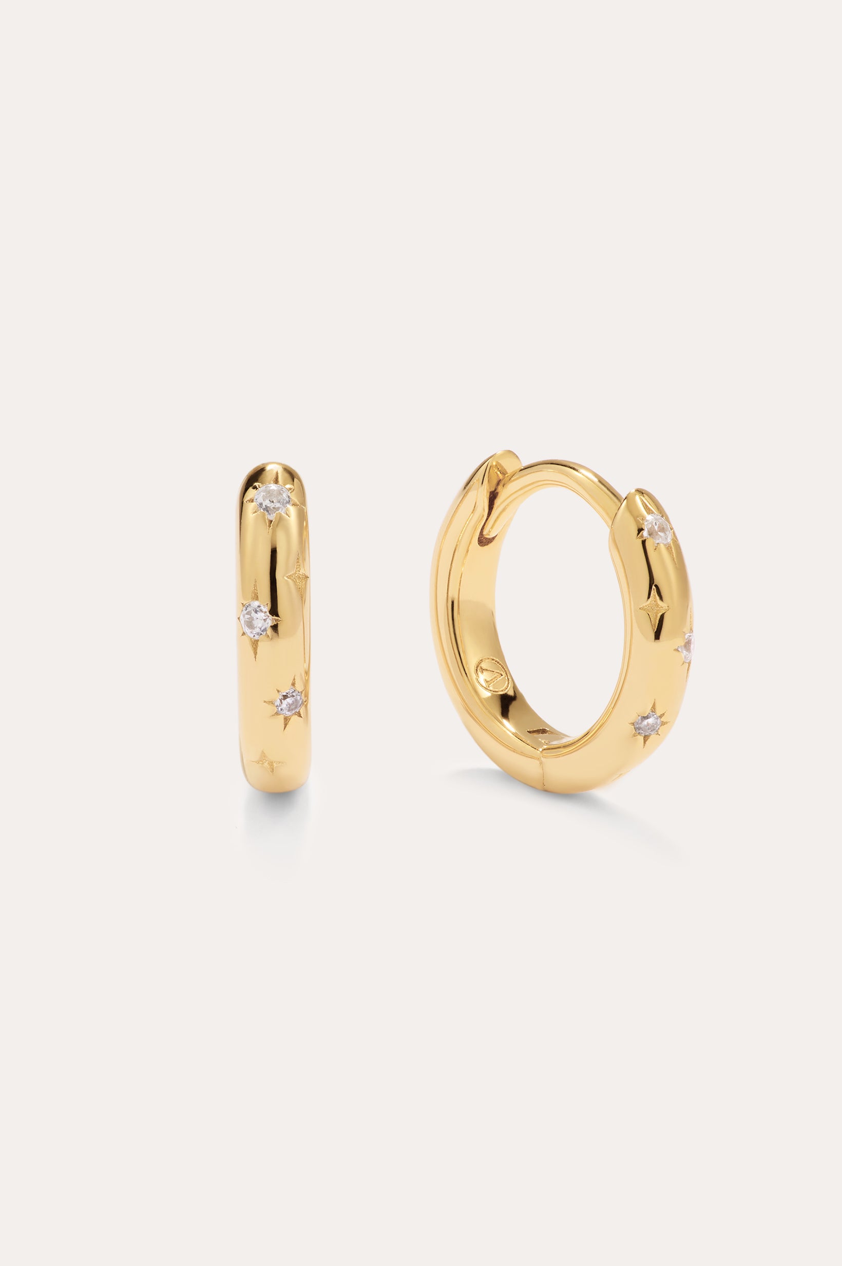 The Starfall Huggies in Gold are a pair of small, 14K gold plated hoops featuring three round clear cubic zirconia stones set within star-shaped engravings—an elegant touch that brings sparkle to any look.