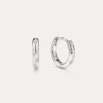 A pair of Starfall Huggies in Silver are displayed against a plain, light background. Crafted in sterling silver, these earrings feature engraved star-shaped designs accented with sparkling cubic zirconia stones, creating a delicate celestial style reminiscent of star burst hoops. The glittering details add an extra touch of brilliance to these elegant pieces.