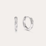 A pair of Starfall Huggies in Silver are displayed against a plain, light background. Crafted in sterling silver, these earrings feature engraved star-shaped designs accented with sparkling cubic zirconia stones, creating a delicate celestial style reminiscent of star burst hoops. The glittering details add an extra touch of brilliance to these elegant pieces.