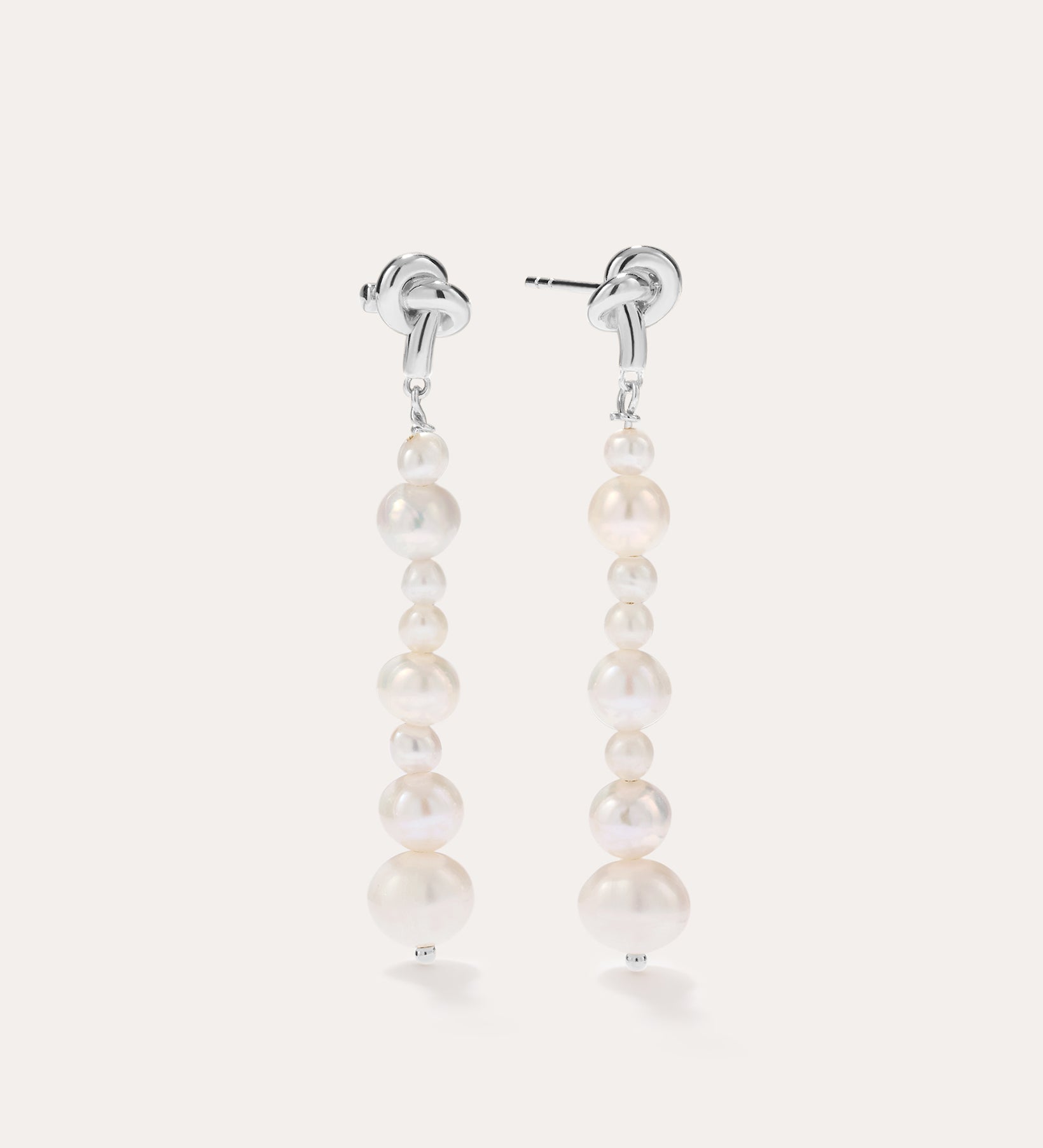 Introducing the Knot Multi Pearl Drop Earrings in Sterling Silver: this pair features a row of lustrous white freshwater pearls in varying sizes, elegantly set on sterling silver posts and showcased against a plain light background.