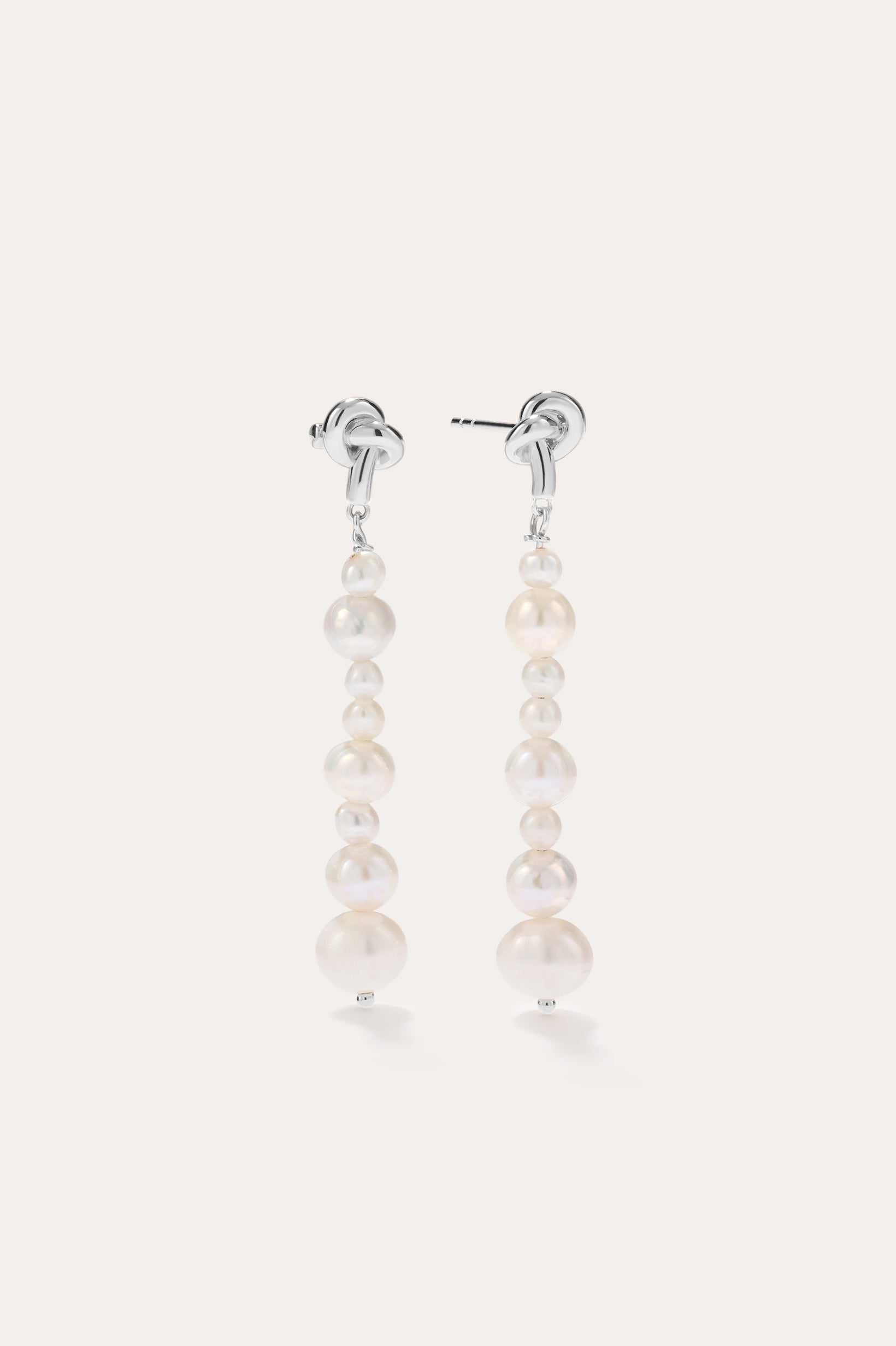 Introducing the Knot Multi Pearl Drop Earrings in Sterling Silver: this pair features a row of lustrous white freshwater pearls in varying sizes, elegantly set on sterling silver posts and showcased against a plain light background.
