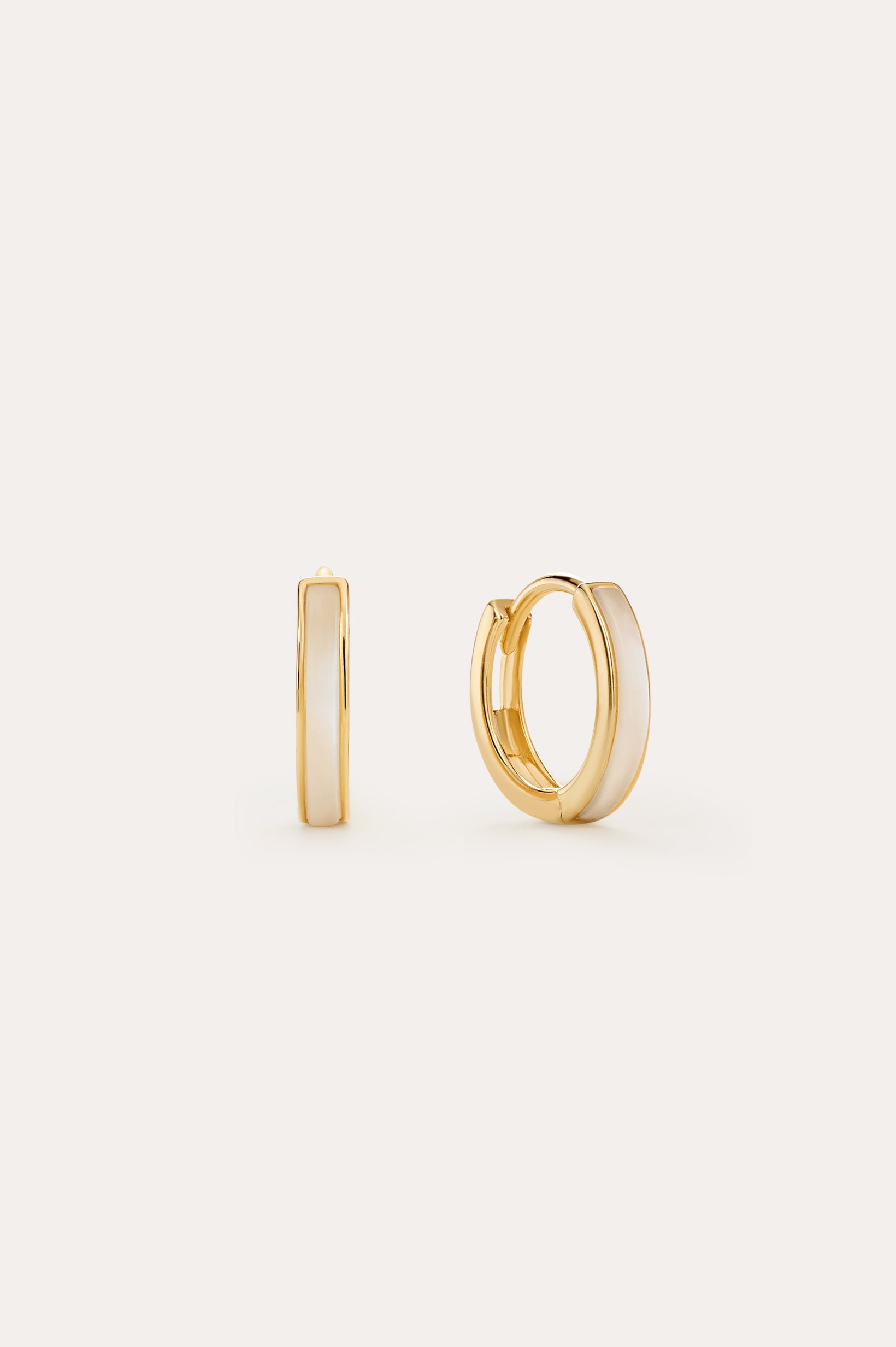 The Mother of Pearl Huggies in Gold are 18k gold-plated small hoops with a glossy white enamel inlay, shown on a light background with one earring facing forward and the other from the side—perfect for everyday jewellery stacks.