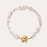 The Flora Multi Pearl Toggle Bracelet in Gold showcases irregular white freshwater pearls and features a 14K gold plated sterling silver butterfly-shaped toggle clasp at the center, elegantly displayed on a light background.