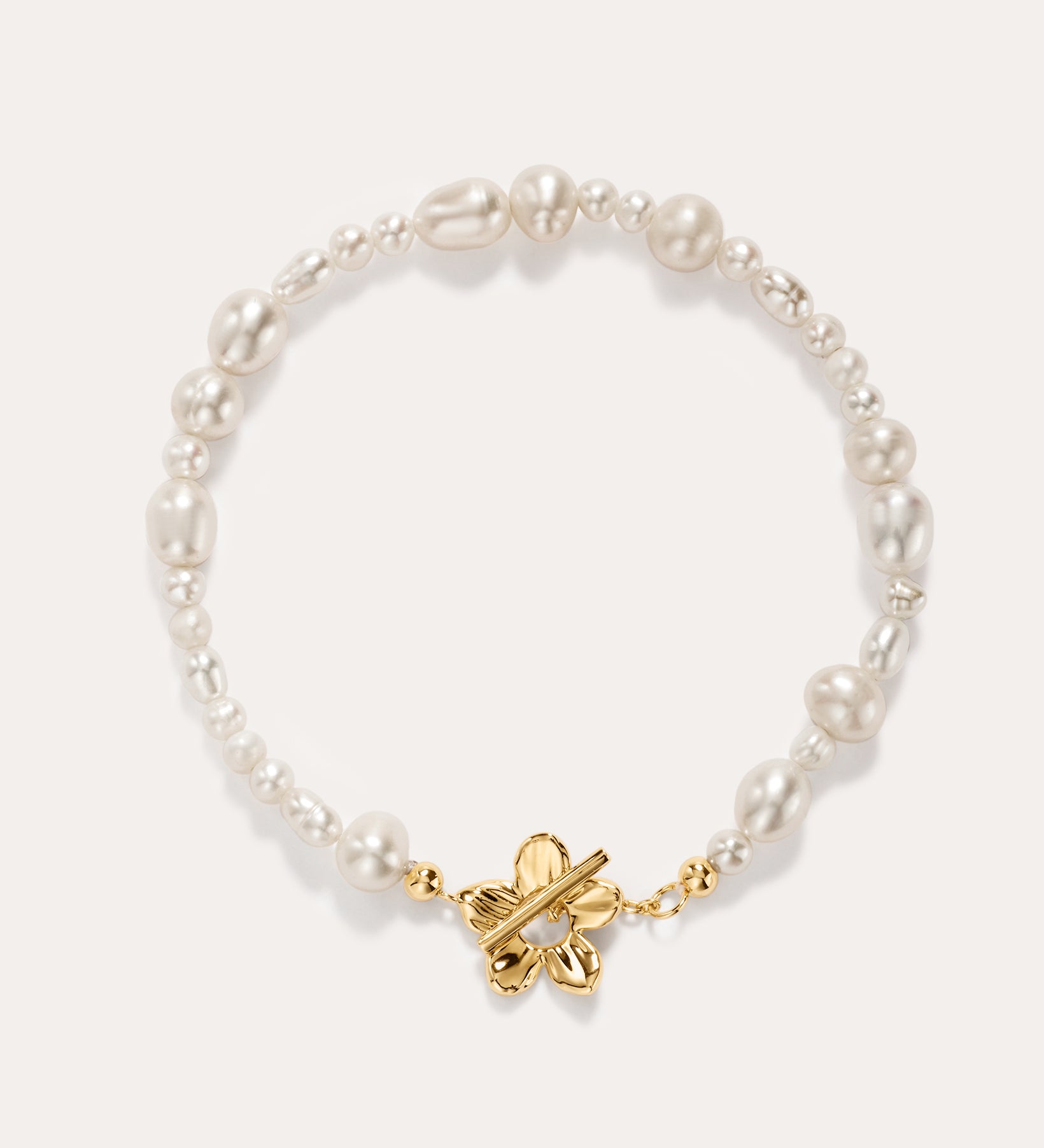 The Flora Multi Pearl Toggle Bracelet in Gold showcases irregular white freshwater pearls and features a 14K gold plated sterling silver butterfly-shaped toggle clasp at the center, elegantly displayed on a light background.