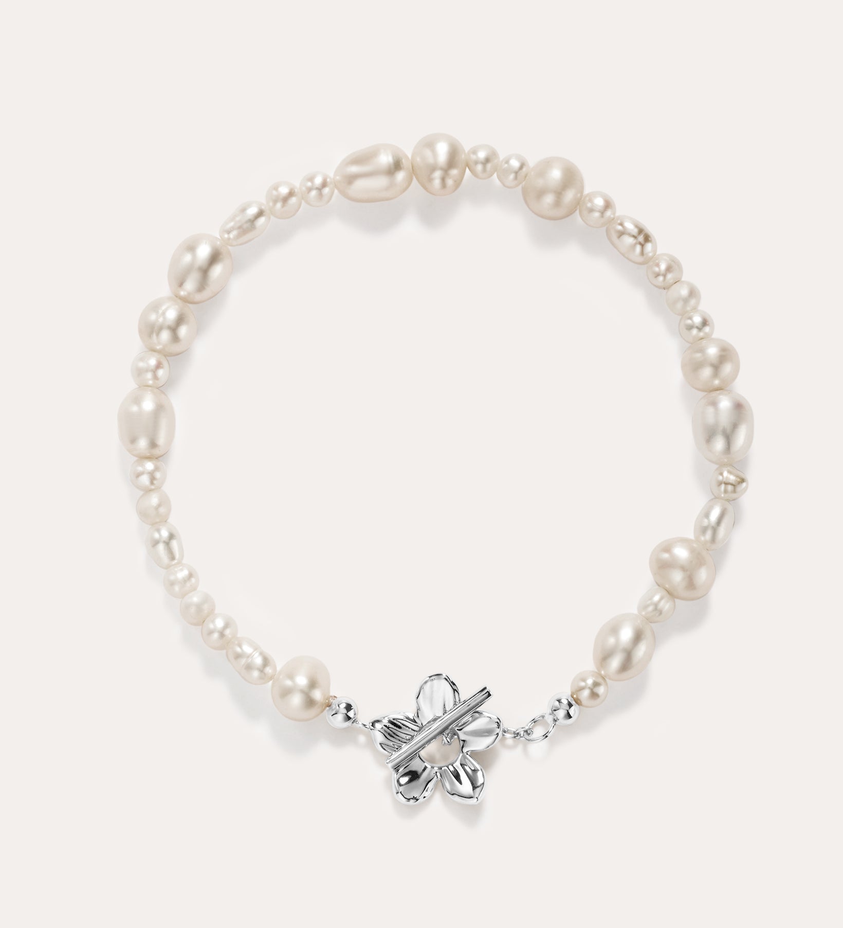 The Flora Multi Pearl Toggle Bracelet in Silver features irregular white freshwater pearls and a sterling silver floral toggle clasp shaped like a butterfly, elegantly displayed on a plain light background.