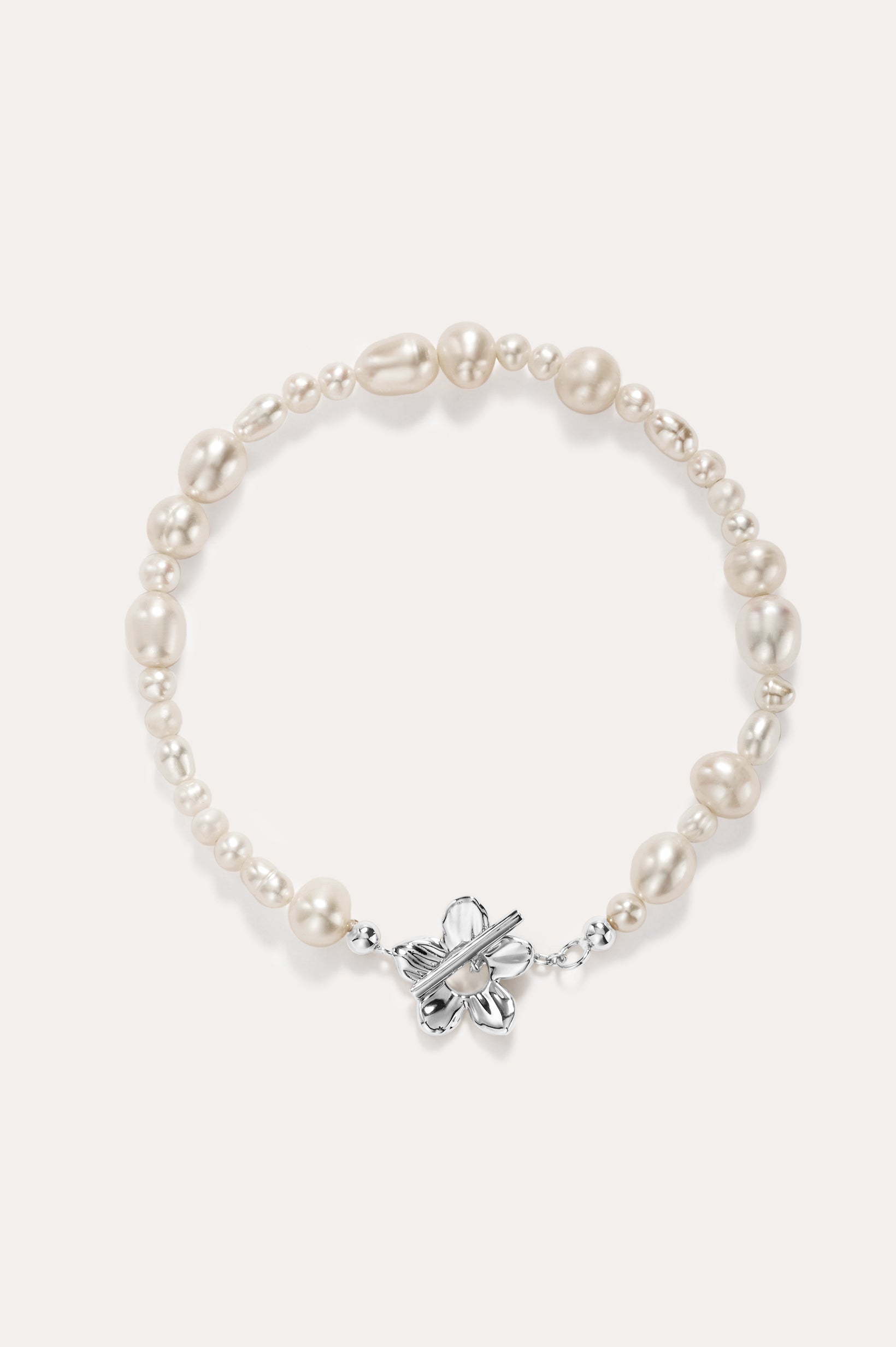 The Flora Multi Pearl Toggle Bracelet in Silver features irregular white freshwater pearls and a sterling silver floral toggle clasp shaped like a butterfly, elegantly displayed on a plain light background.