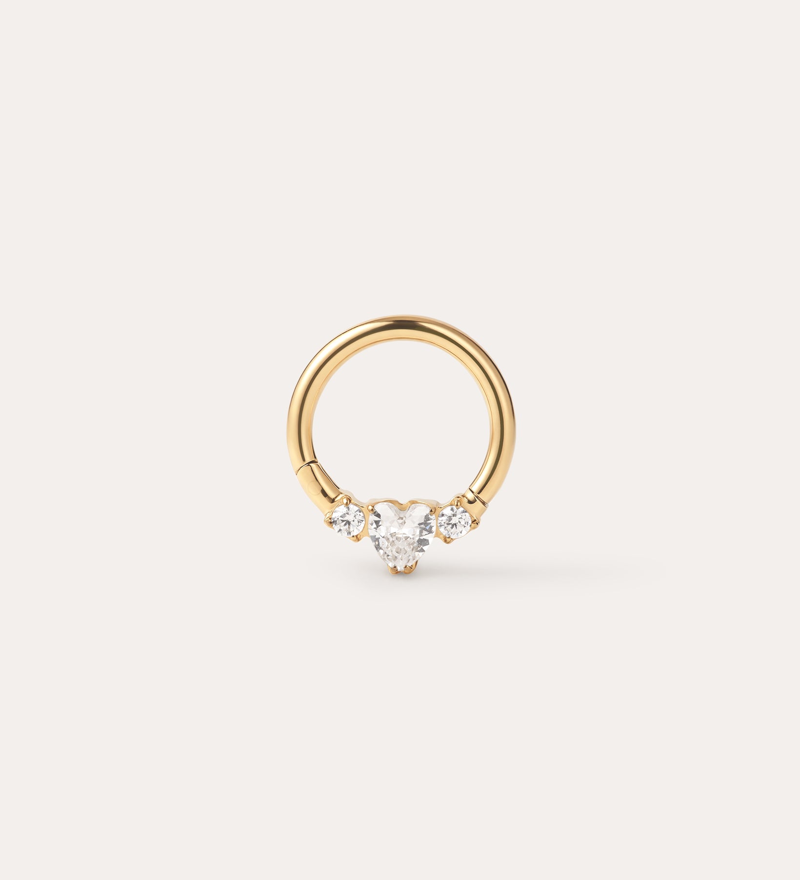 The Crystal Heart Titanium Daith Ring in Gold features a petite gold hoop with a pear-shaped clear gemstone at its center, accented by two round clear stones on each side, shown against a simple light background—ideal for sensitive ears thanks to its hypoallergenic Yellow Gold PVD finish.