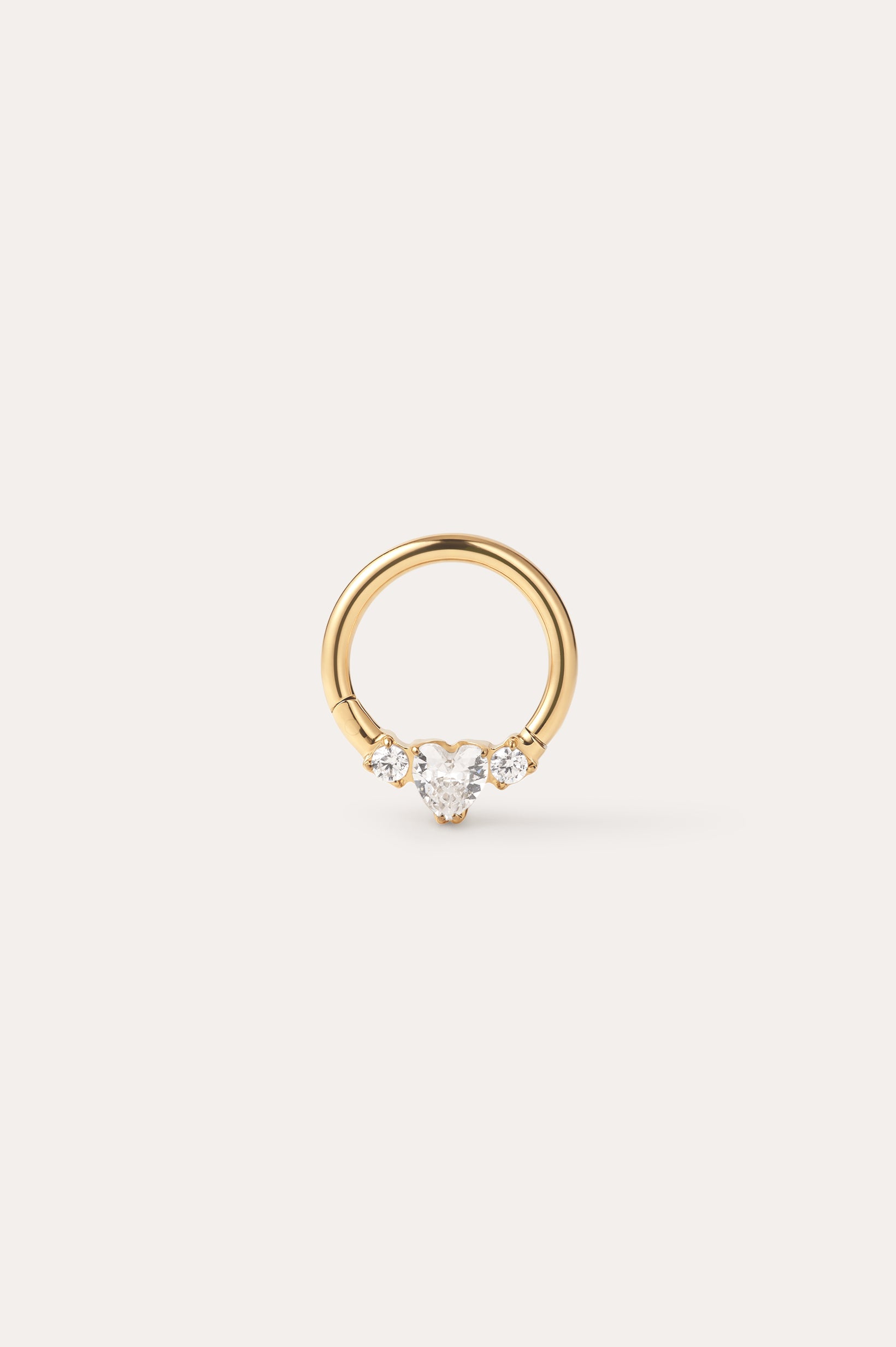 The Crystal Heart Titanium Daith Ring in Gold features a petite gold hoop with a pear-shaped clear gemstone at its center, accented by two round clear stones on each side, shown against a simple light background—ideal for sensitive ears thanks to its hypoallergenic Yellow Gold PVD finish.