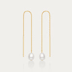 The Eira Pearl Drop Threader Earrings in Gold feature delicate chains ending with a single round white pearl, offering a minimalist and elegant look against a plain white background.