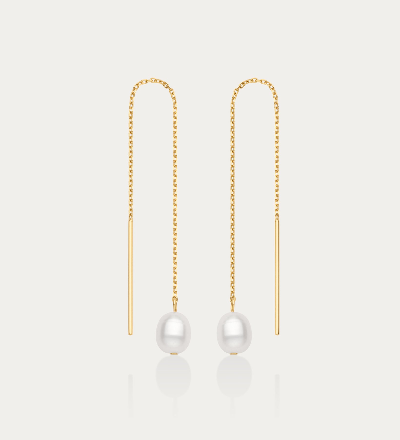 The Eira Pearl Drop Threader Earrings in Gold feature delicate chains ending with a single round white pearl, offering a minimalist and elegant look against a plain white background.