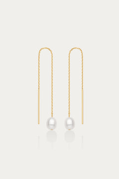 The Eira Pearl Drop Threader Earrings in Gold feature delicate chains ending with a single round white pearl, offering a minimalist and elegant look against a plain white background.