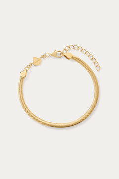 The Estelle Herringbone Chain Bracelet in Gold is a 3mm bracelet with an adjustable clasp, extension chain, and a small flat charm, perfect for bracelet stacking and shown on a light background.