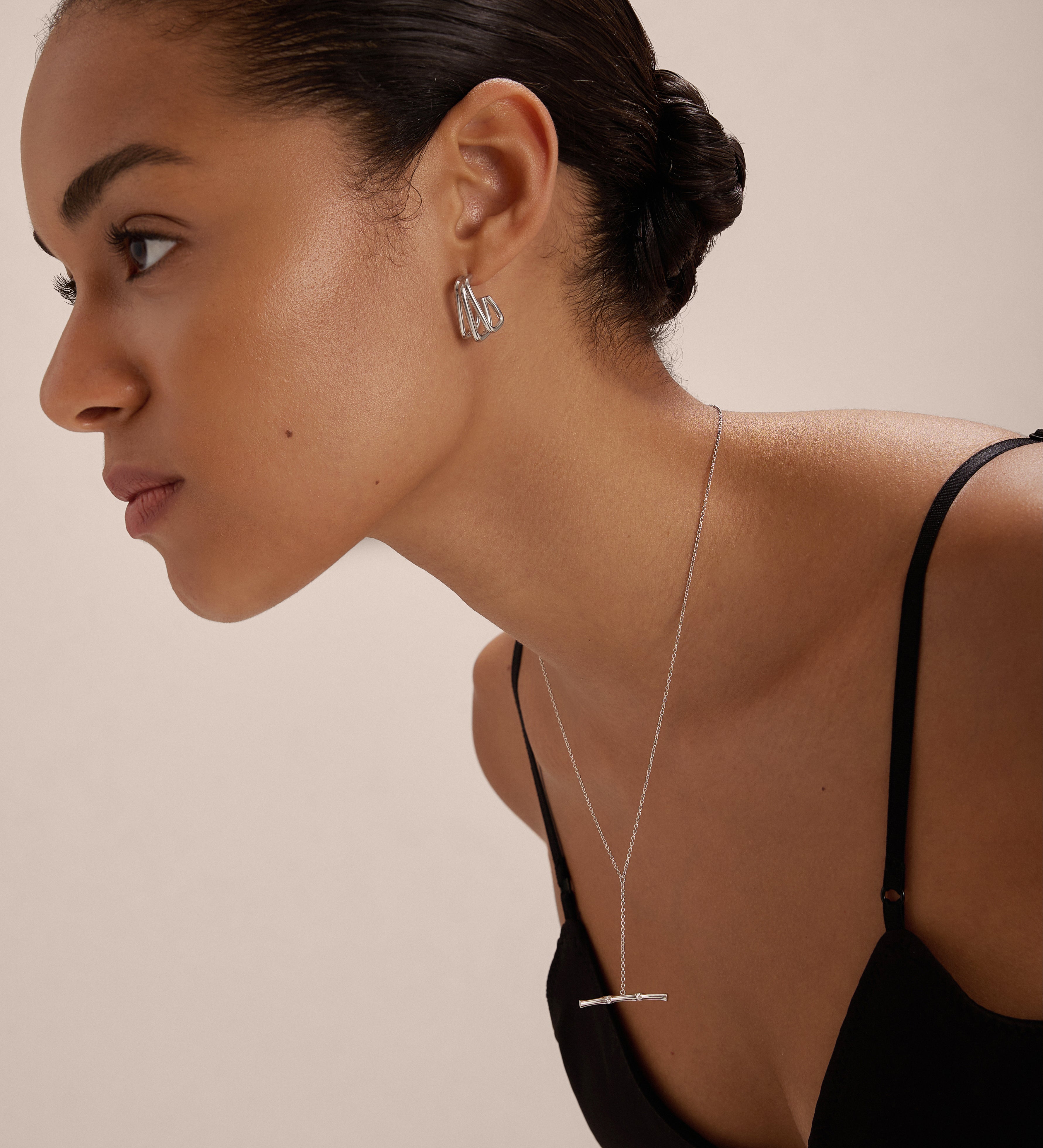 A woman with smooth, pulled-back hair wears a black spaghetti strap top and Esther Square Hoop Stud Earrings in Silver, paired with a delicate silver bar necklace, posing against a plain light background.