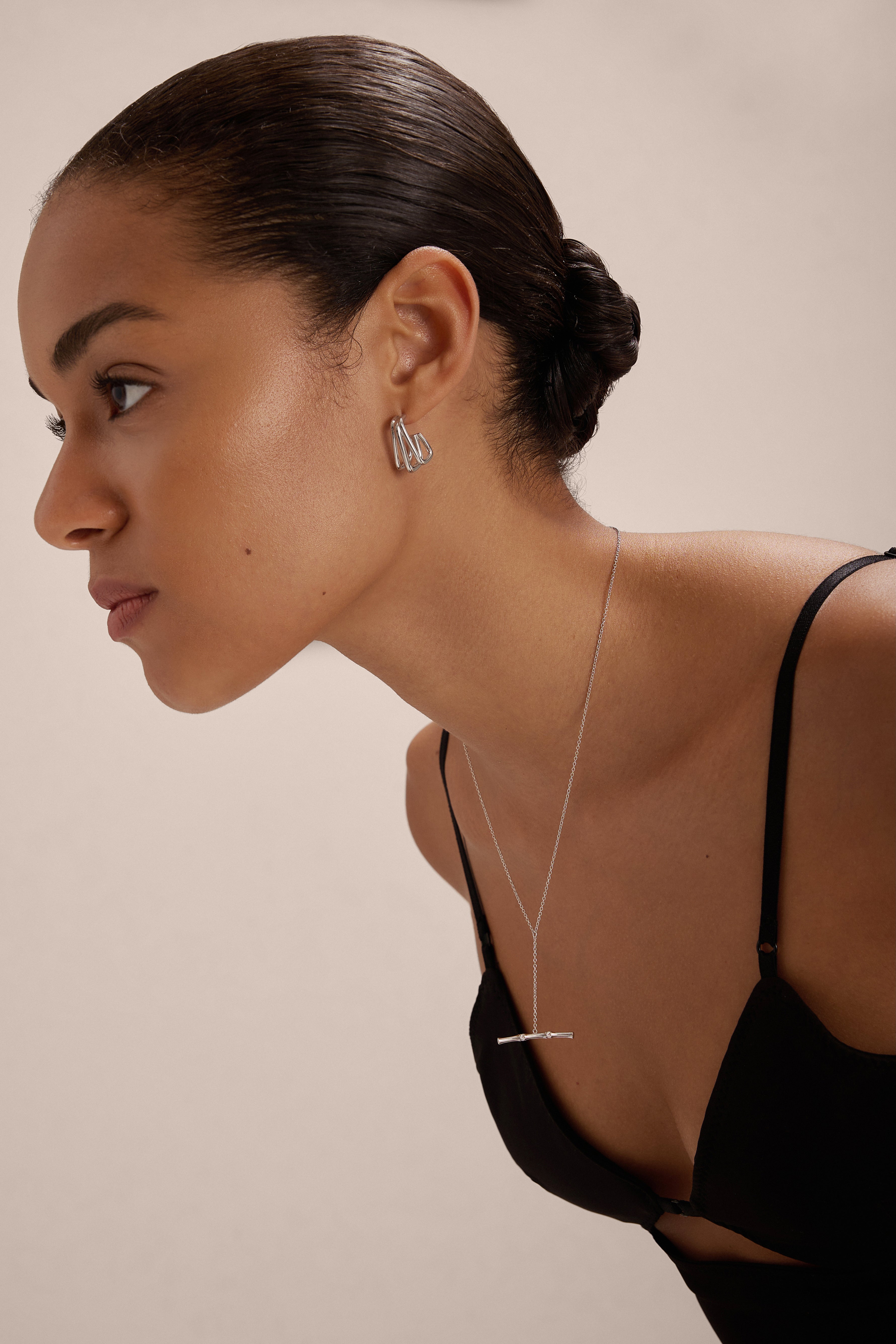 A woman with smooth, pulled-back hair wears a black spaghetti strap top and Esther Square Hoop Stud Earrings in Silver, paired with a delicate silver bar necklace, posing against a plain light background.
