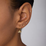 Close-up of an ear adorned with multiple gold earrings, featuring Defender Evil Eye Hoops in Gold with pearl details on the lobe and small protective jewelry along the cartilage.