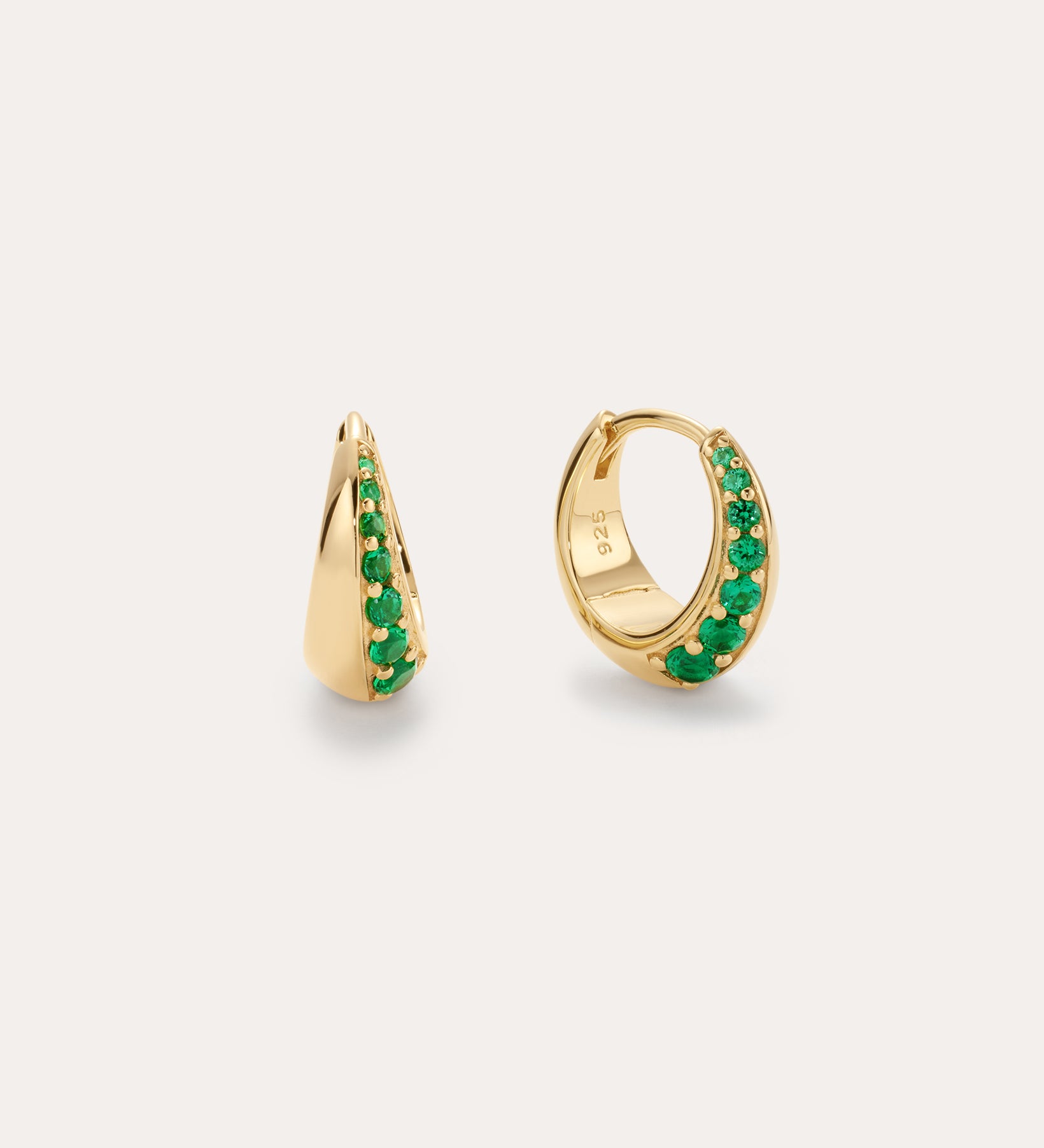 The Georgie Crystal Knife Edge Huggie Hoop Earrings in Green feature small gold hoops with a row of green crystals along the front, shown against a plain light background.