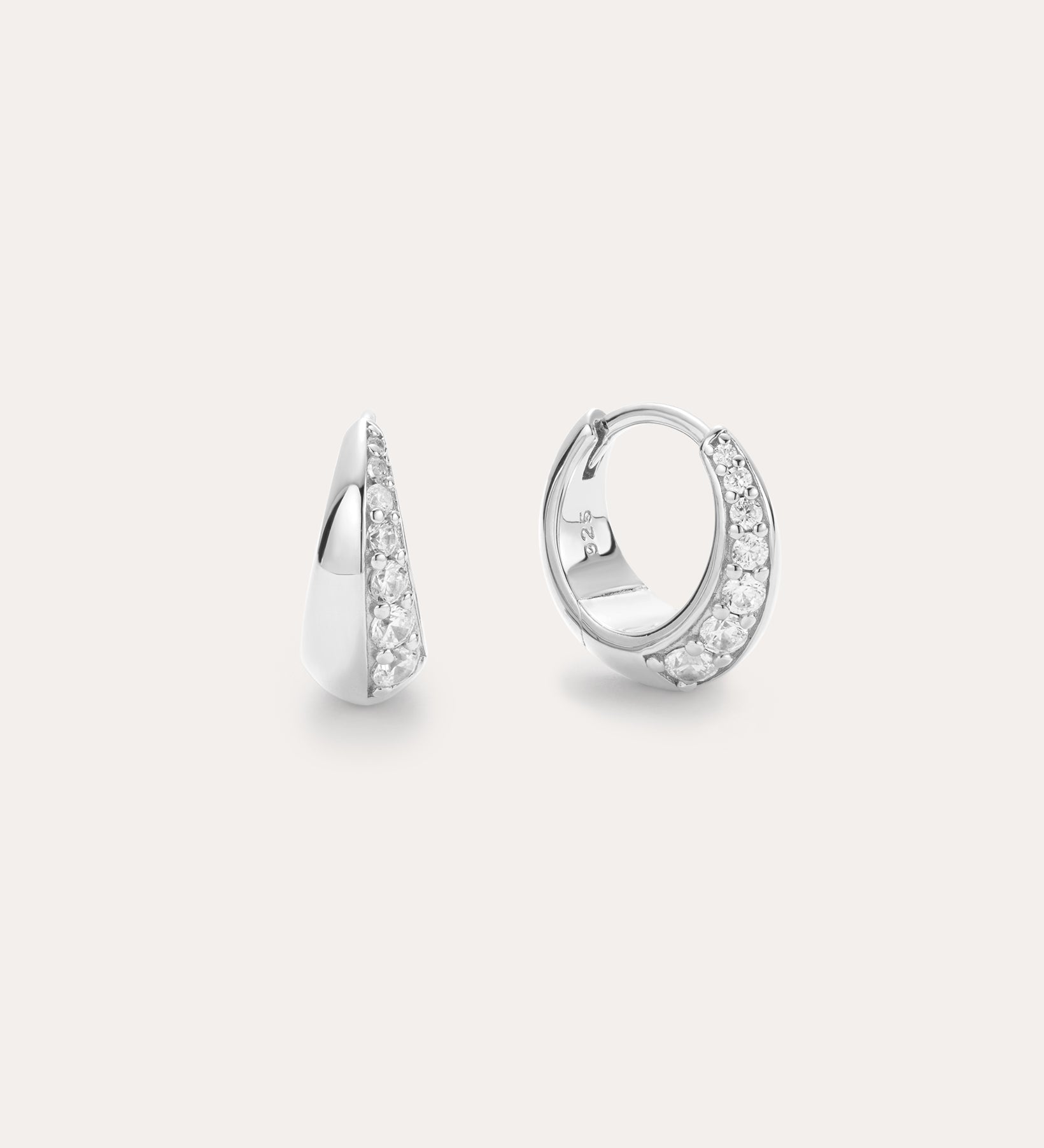 The Georgie Crystal Knife Edge Huggie Hoop Earrings in Silver feature a row of sparkling white stones, shown on a plain light background with one earring displayed from the front and the other from the side.
