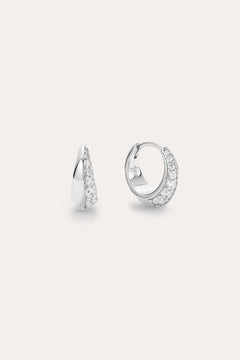 The Georgie Crystal Knife Edge Huggie Hoop Earrings in Silver feature a row of sparkling white stones, shown on a plain light background with one earring displayed from the front and the other from the side.