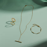 A delicate gold jewelry set arranged on a mint green surface, featuring a ring, bracelet, and the Bamboo Chain Y-Bar Lariat Necklace in Gold, each piece casting soft shadows.
