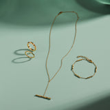 A delicate gold jewelry set arranged on a mint green surface, featuring a ring, bracelet, and the Bamboo Chain Y-Bar Lariat Necklace in Gold, each piece casting soft shadows.