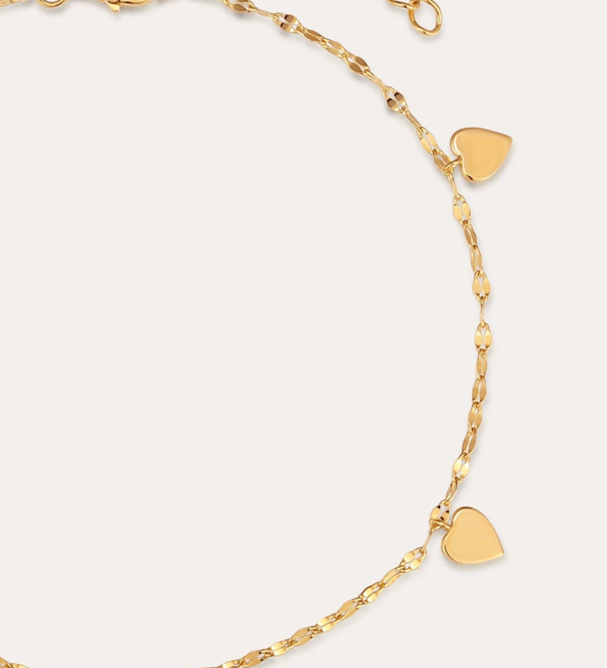 The Louise Gold Heart Anklet features four small gold hearts and a central heart with clear stones on a delicate gold chain. With an adjustable clasp, it can also be worn as a bracelet. Displayed on a plain light background.
