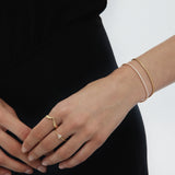 A person in black showcases their left hand with the Veda Plain Chevron Ring in Gold, plus two gold bracelets, against a plain white background.
