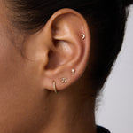 A close-up of an ear with four gold earrings: a crescent moon stud in the upper cartilage, 14K Recycled Solid Yellow Gold Rope Huggie Earrings in the lobe, and two small shaped studs above the huggie.