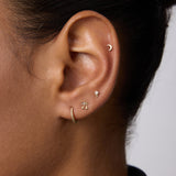 A close-up of an ear with four gold earrings: a crescent moon stud in the upper cartilage, 14K Recycled Solid Yellow Gold Rope Huggie Earrings in the lobe, and two small shaped studs above the huggie.