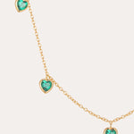 The Thea Green Heart Pendant Gold Necklace is a delicate adjustable gold chain adorned with five evenly spaced, small green cubic zirconia heart-shaped gemstones.