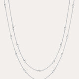 The Simona Double Chain Stacking Necklace in Silver features two delicate layers with small, evenly spaced beads along each chain, shown against a light background.