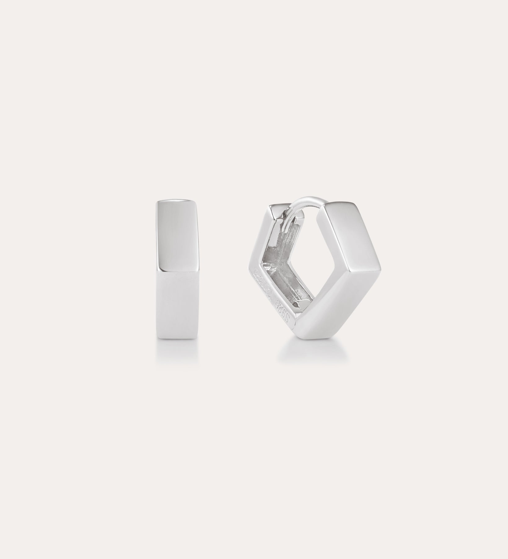 The Judith Hexagon Angular Huggies in Silver, featuring a chunky geometric design, are shown on a plain light background—one upright and one open to reveal the clasp. Perfect for stacking earring looks.