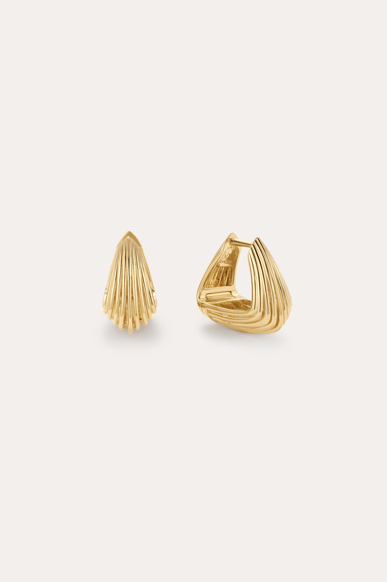 The Juno Ridged Chunky Hoops in Gold feature a modern, shell-inspired design. Displayed on a light background, one hoop stands upright while the other is open to showcase the clasp.