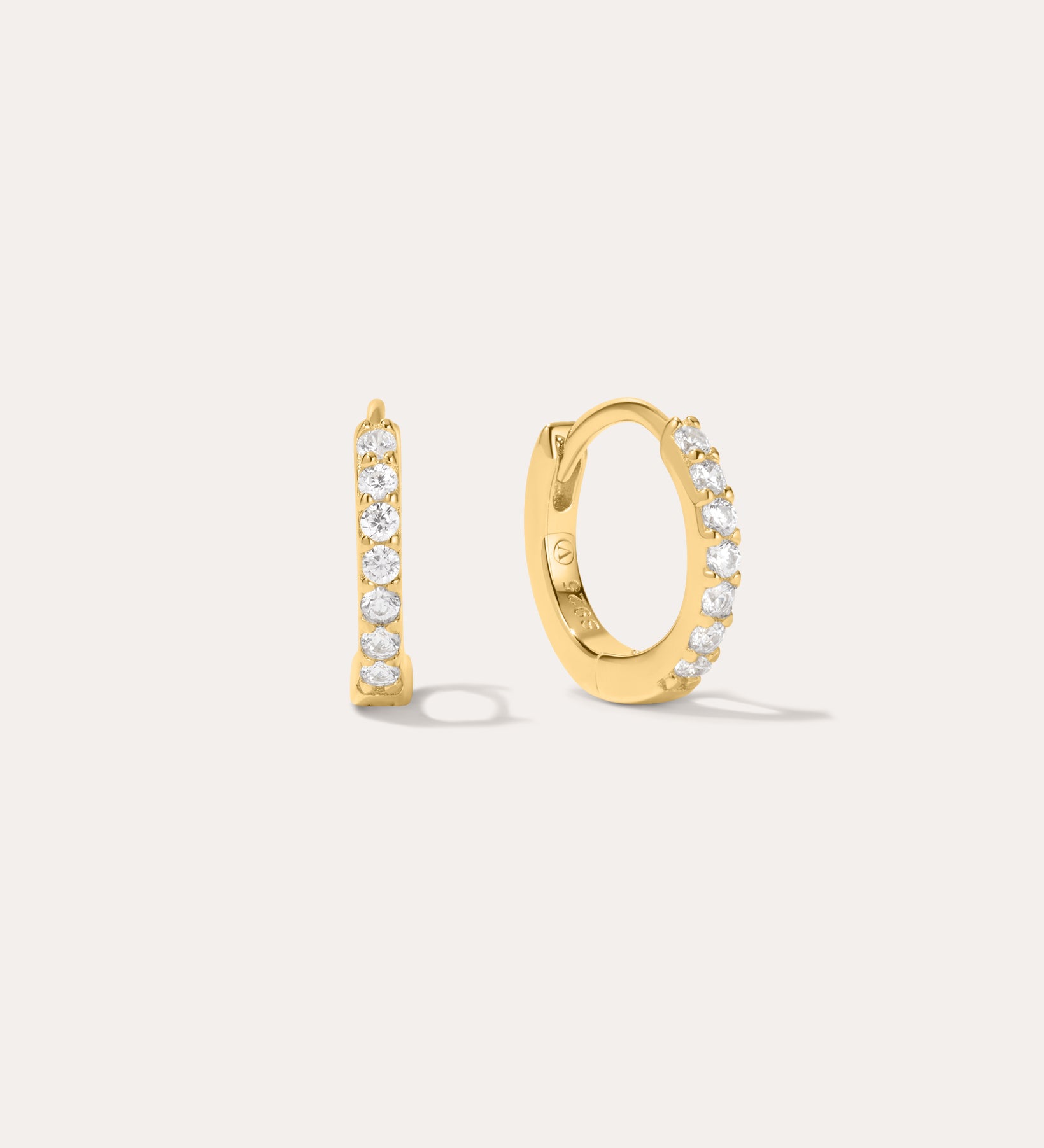 The Kiki Crystal Huggie Earrings in Gold feature a row of clear round crystals on 18k gold-plated hoops. One earring is shown from the side, the other from the front, against a light background—ideal for stacking.