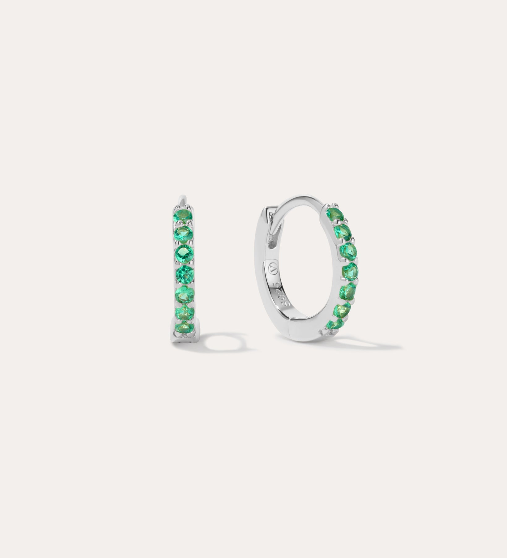 The Kiki Crystal Huggie Earrings in Sterling Silver/Green are displayed on a white background, with one earring facing forward and the other shown from the side.