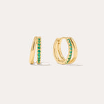 The Kira Crystal Double Hoop Huggies in Gold/Green are small earrings featuring a row of shimmering gemstones on the front, displayed against a plain light background.