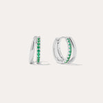 The Kira Crystal Double Hoop Huggies in Sterling Silver/Green feature a row of green gemstones along the front and are displayed against a plain white background.