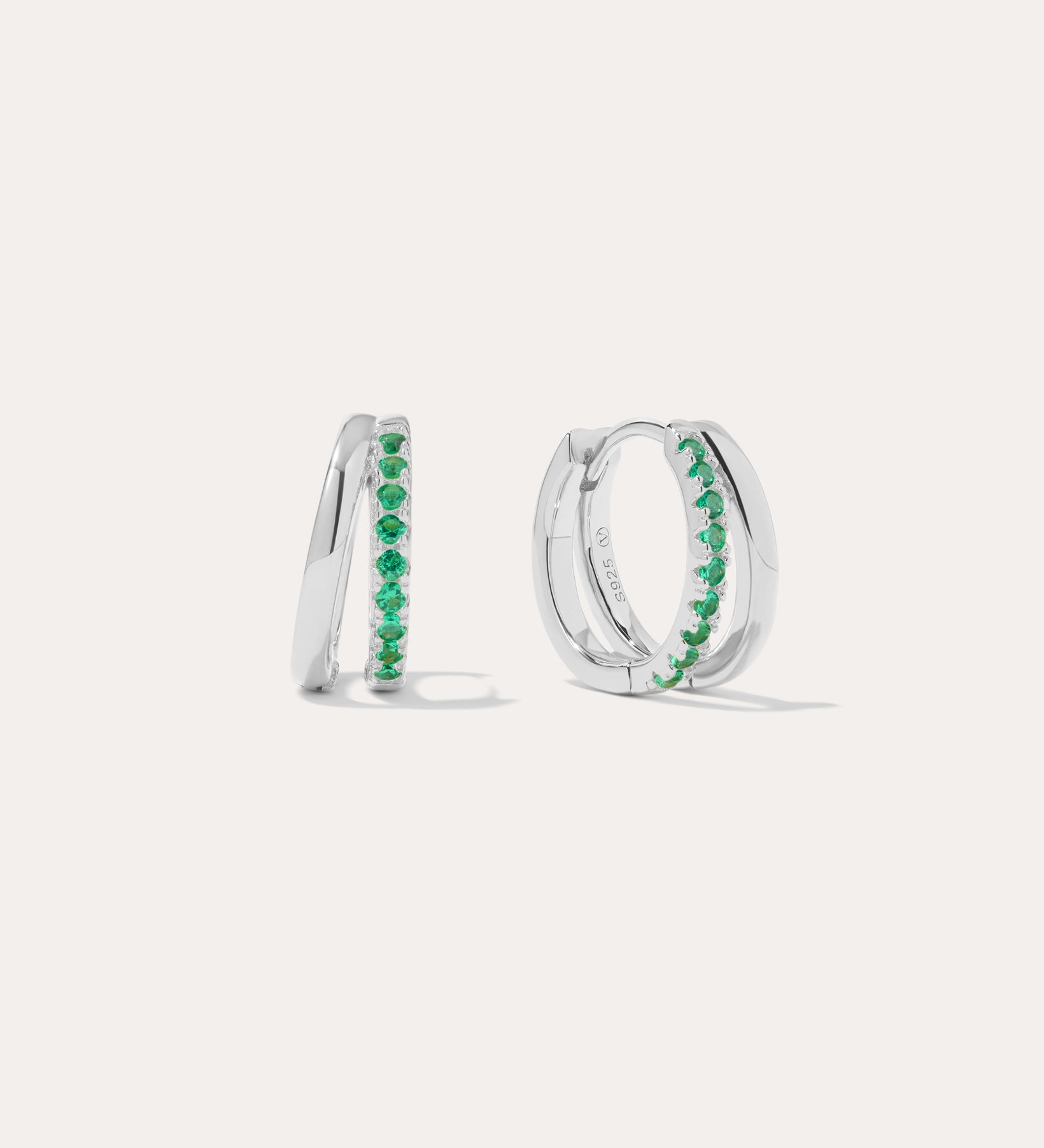 The Kira Crystal Double Hoop Huggies in Sterling Silver/Green feature a row of green gemstones along the front and are displayed against a plain white background.