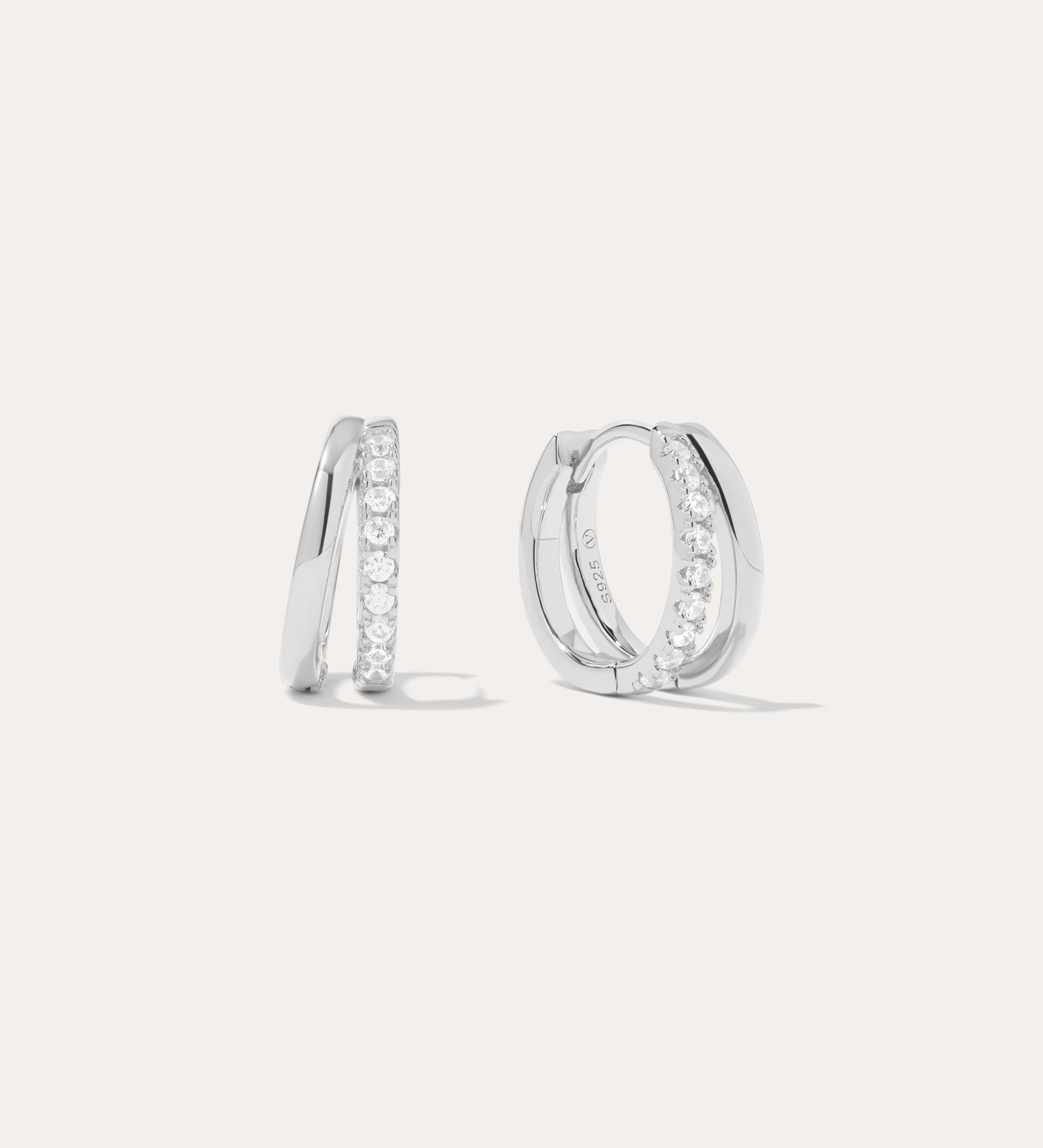 The Kira Crystal Double Hoop Huggies in Sterling Silver are shown, each featuring a row of sparkling round crystals along the front edge. The background is plain and light-colored.